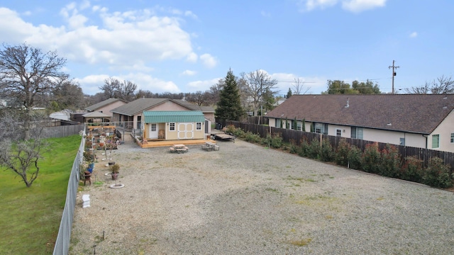 back of property featuring a deck, a fenced backyard, a yard, gravel driveway, and an outdoor structure