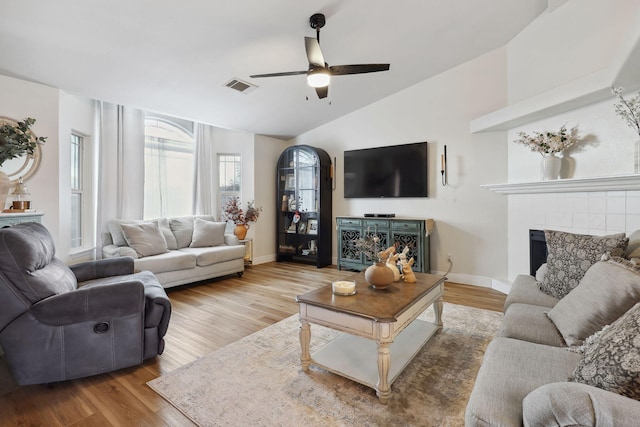 living room featuring visible vents, a tiled fireplace, wood finished floors, ceiling fan, and vaulted ceiling