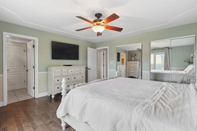 bedroom featuring ceiling fan, wood finished floors, multiple closets, and baseboards