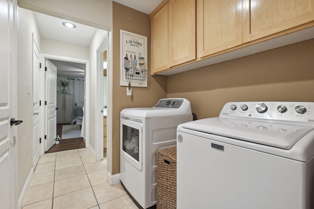 clothes washing area with washing machine and clothes dryer, light tile patterned floors, cabinet space, and baseboards