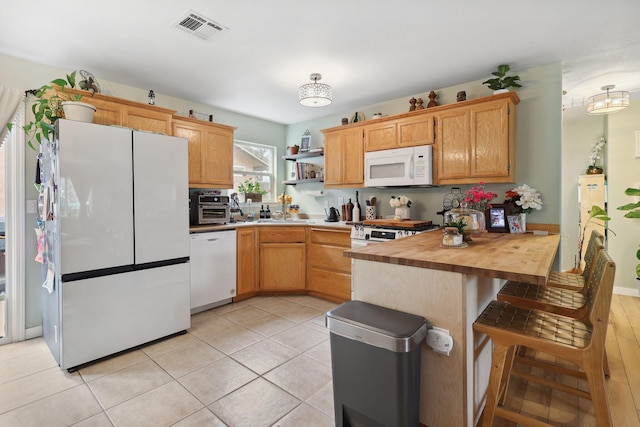 kitchen featuring visible vents, wooden counters, a kitchen breakfast bar, a peninsula, and white appliances