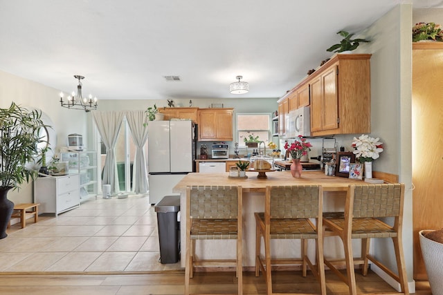 kitchen with visible vents, white appliances, a peninsula, light tile patterned floors, and a chandelier