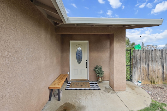 entrance to property featuring stucco siding and fence