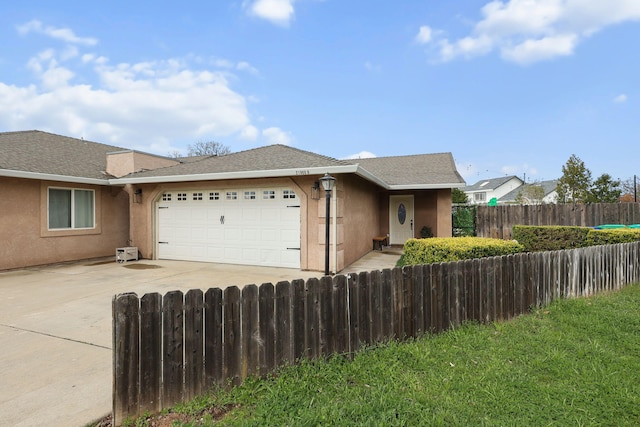 ranch-style home featuring an attached garage, a shingled roof, stucco siding, concrete driveway, and a fenced front yard