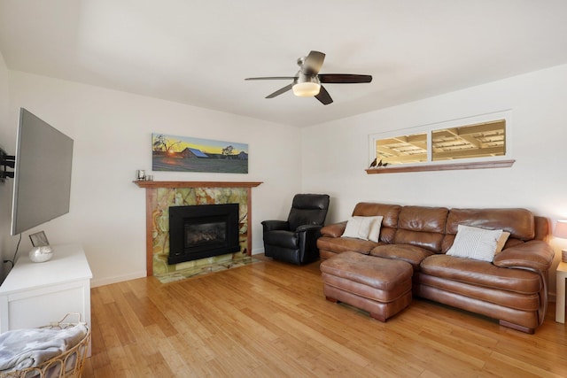 living area featuring light wood-style flooring, baseboards, a tile fireplace, and ceiling fan