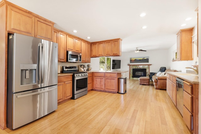 kitchen featuring open floor plan, light wood-style flooring, appliances with stainless steel finishes, a peninsula, and a ceiling fan