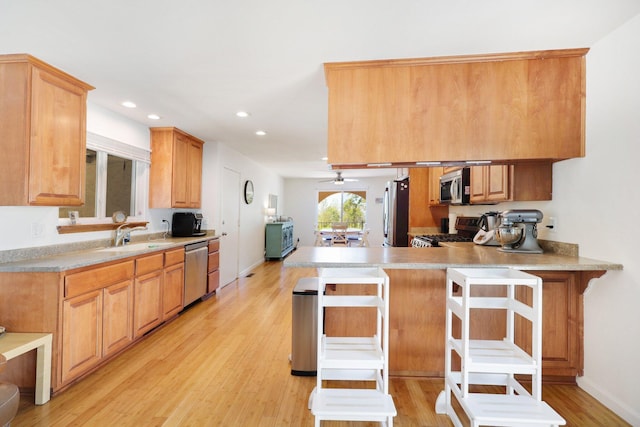 kitchen featuring light wood-style flooring, a sink, recessed lighting, appliances with stainless steel finishes, and a peninsula