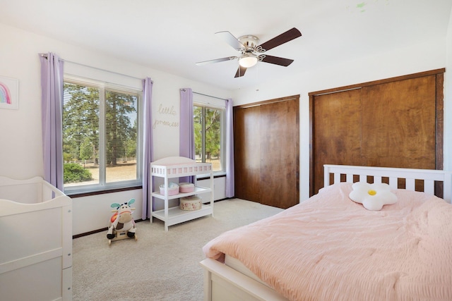 bedroom featuring ceiling fan, multiple windows, two closets, and light carpet