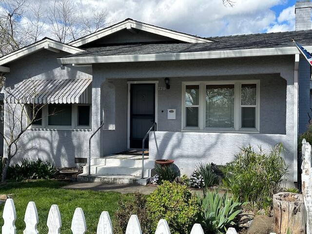 bungalow-style house with stucco siding, a porch, and a shingled roof