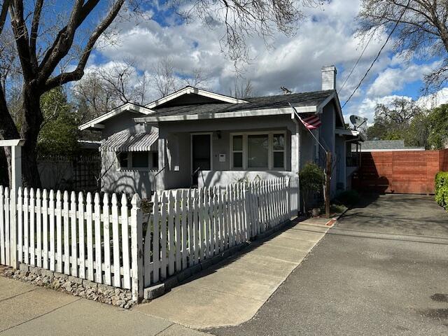 bungalow with a fenced front yard, covered porch, and a chimney