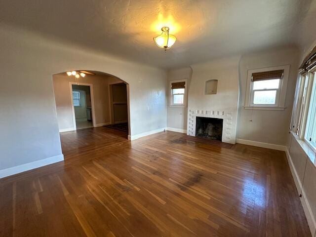 unfurnished living room with baseboards, arched walkways, wood finished floors, and a fireplace