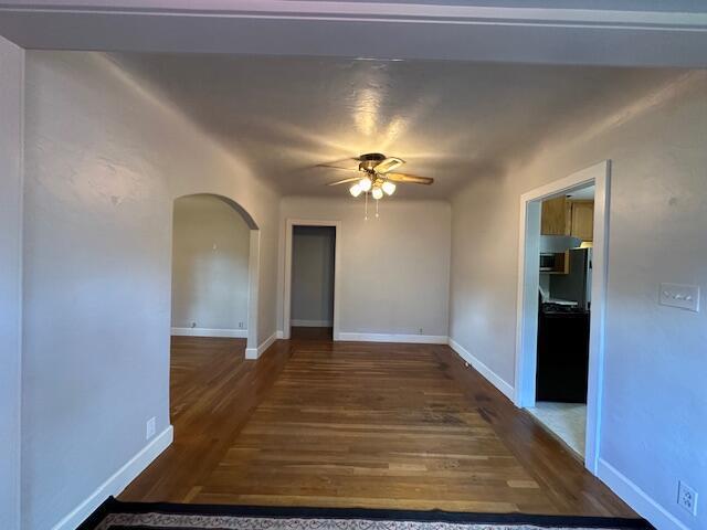 empty room with arched walkways, baseboards, ceiling fan, and wood finished floors