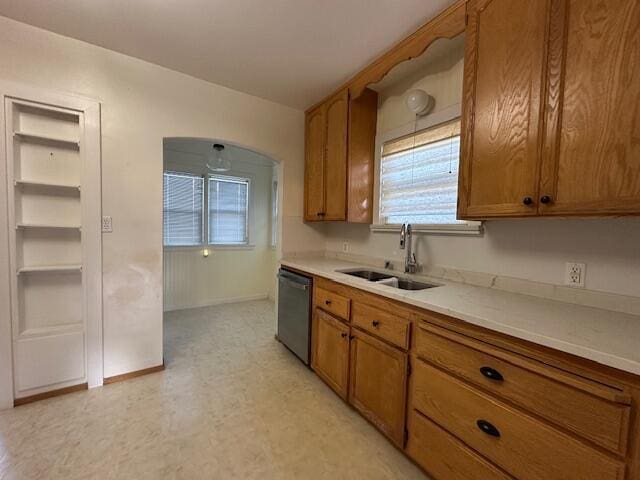 kitchen featuring light floors, light countertops, stainless steel dishwasher, brown cabinetry, and a sink