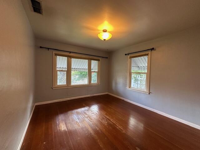 spare room with dark wood-type flooring, baseboards, visible vents, and a healthy amount of sunlight