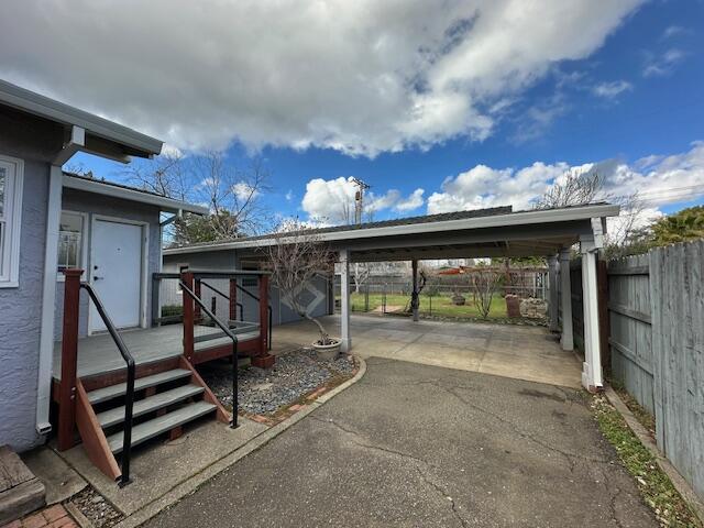 view of vehicle parking with an attached carport, driveway, and fence