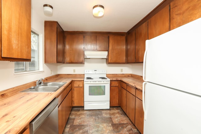 kitchen with brown cabinets, stone finish floor, under cabinet range hood, a sink, and white appliances