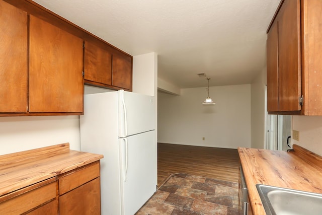 kitchen with brown cabinetry, butcher block counters, and freestanding refrigerator