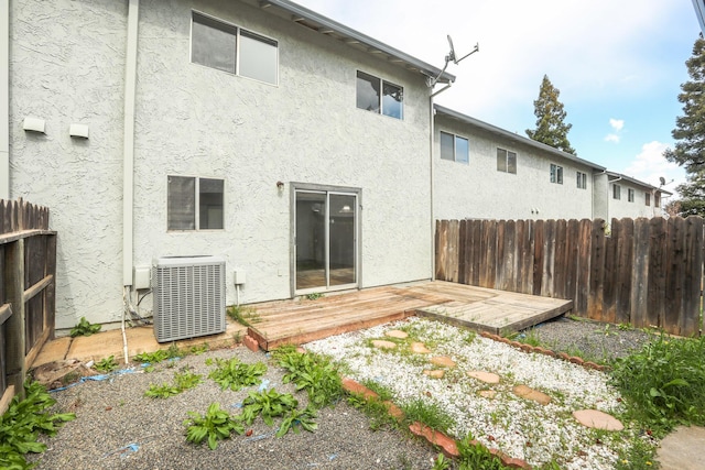 rear view of property with a wooden deck, fence, central AC unit, and stucco siding