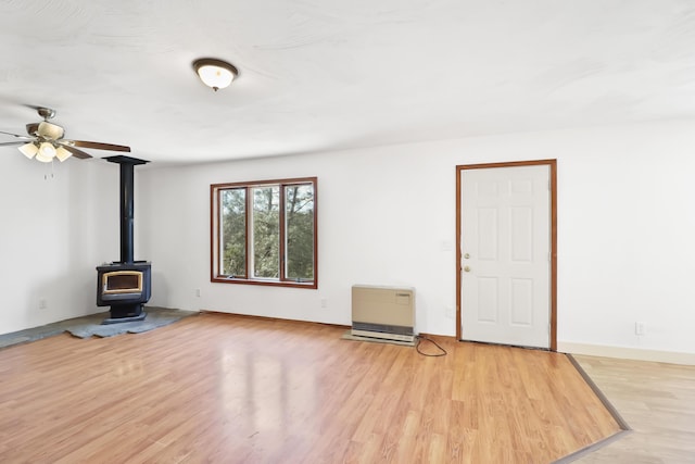 unfurnished living room featuring ceiling fan, heating unit, light wood-style flooring, and a wood stove