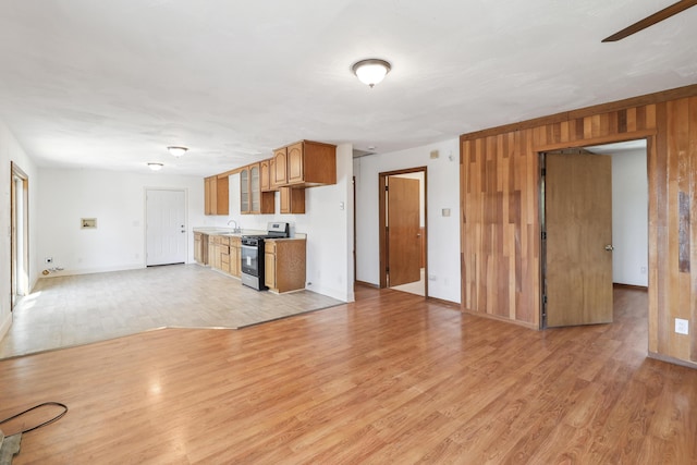 kitchen with range with gas stovetop, wooden walls, light wood-style flooring, a sink, and open floor plan