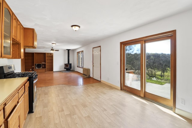 kitchen with brown cabinetry, a wood stove, light wood-style floors, glass insert cabinets, and gas range