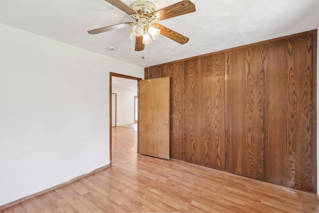 unfurnished room with light wood-type flooring, baseboards, ceiling fan, and wood walls