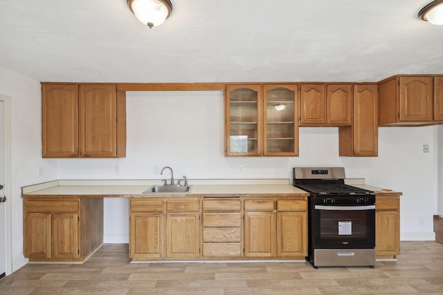 kitchen with a sink, brown cabinetry, light wood-style floors, and stainless steel gas range oven