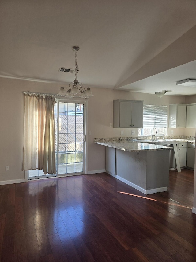 kitchen with visible vents, decorative light fixtures, a peninsula, baseboards, and dark wood-style flooring