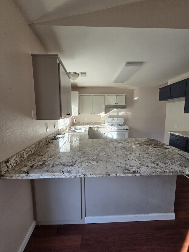 kitchen featuring a sink, light stone counters, a peninsula, and white gas range