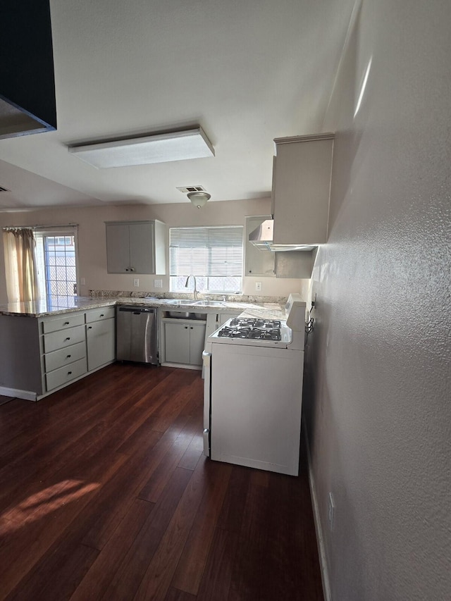 kitchen with dark wood finished floors, gas range, dishwasher, a peninsula, and a textured wall