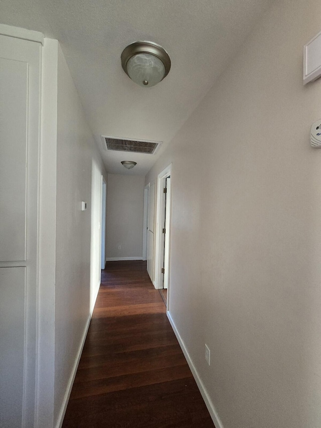 hall with visible vents, baseboards, and wood finished floors
