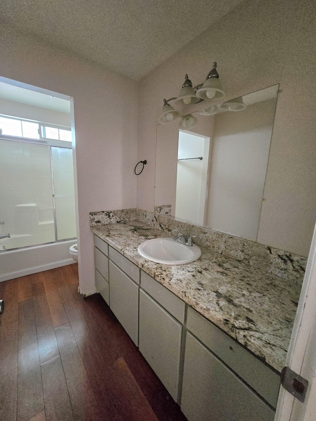 bathroom featuring toilet, a textured ceiling, wood finished floors, enclosed tub / shower combo, and vanity