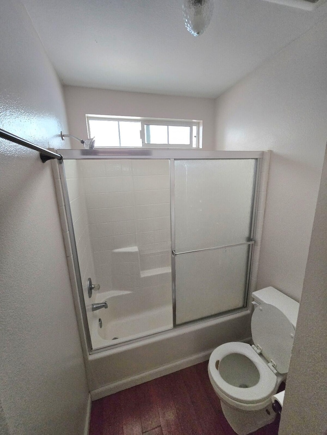 bathroom with toilet, wood finished floors, and combined bath / shower with glass door