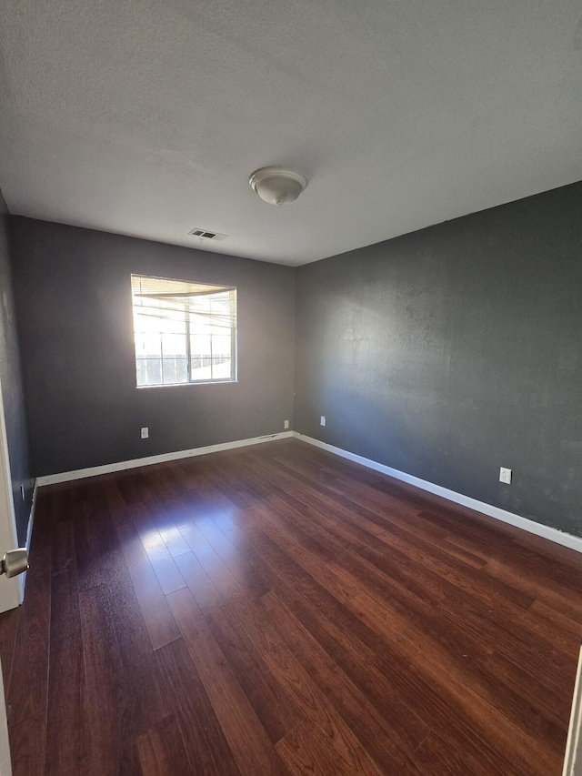 unfurnished room with a textured ceiling, wood finished floors, visible vents, and baseboards
