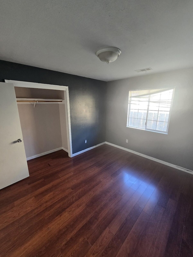 unfurnished bedroom featuring visible vents, baseboards, a closet, and dark wood finished floors