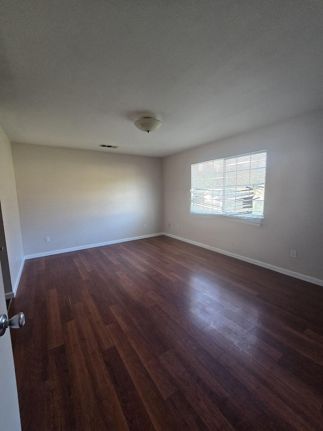 unfurnished room with visible vents, baseboards, and dark wood finished floors