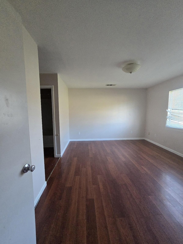 empty room featuring baseboards, dark wood-style flooring, and a textured ceiling