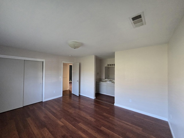 unfurnished bedroom featuring dark wood finished floors, visible vents, a closet, and baseboards