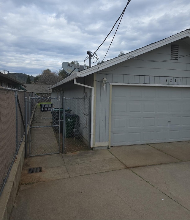garage featuring concrete driveway, a gate, and fence