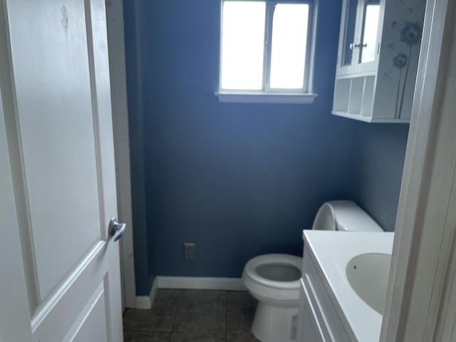 half bath with toilet, tile patterned floors, vanity, and baseboards
