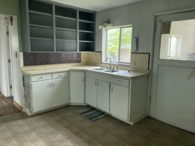 kitchen featuring white cabinetry, open shelves, light countertops, a sink, and decorative backsplash