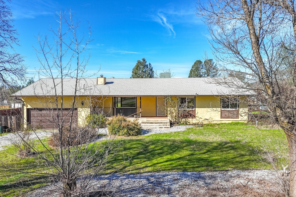 ranch-style house with a porch, a chimney, stucco siding, a front lawn, and a garage
