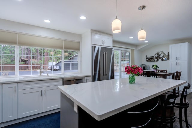 kitchen featuring white cabinets, a kitchen island, appliances with stainless steel finishes, light stone counters, and pendant lighting