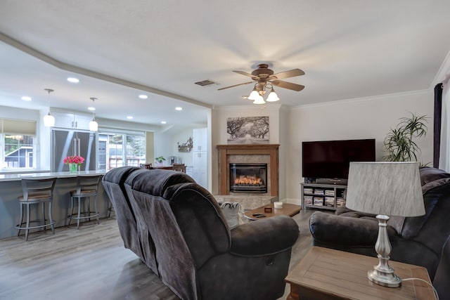 living room featuring visible vents, crown molding, ceiling fan, a tiled fireplace, and light wood-type flooring