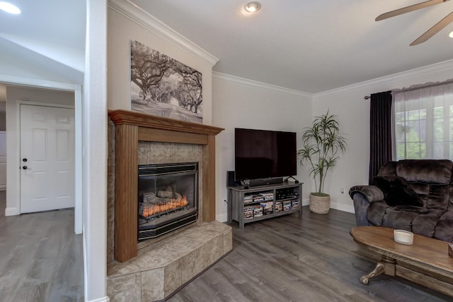 living area with crown molding, a fireplace, wood finished floors, baseboards, and ceiling fan