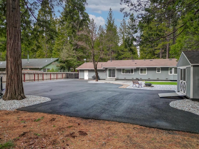 back of house featuring an outbuilding, fence, an outdoor fire pit, a patio area, and a storage shed