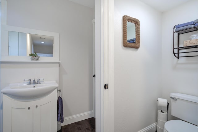 half bath with toilet, vanity, baseboards, and wood finished floors