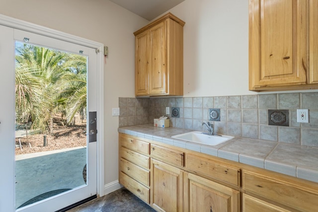 kitchen featuring tile counters, light brown cabinetry, baseboards, backsplash, and a sink