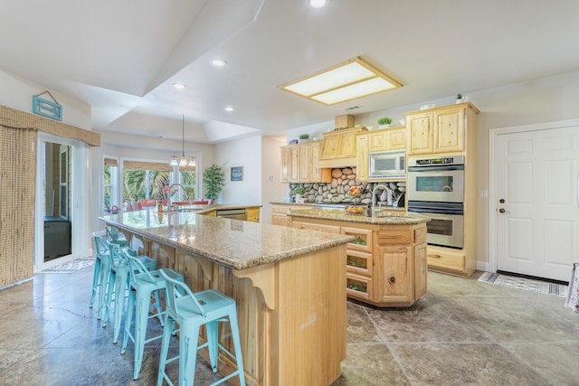 kitchen with stainless steel appliances, tasteful backsplash, light brown cabinets, a sink, and a large island