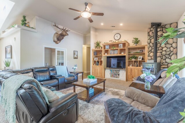 living area with a ceiling fan, a wood stove, lofted ceiling, visible vents, and carpet
